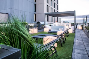 An outdoor seating area with tables and chairs, a grill, and a view of the cityscape. - 33 Parkside - Coventry (Coventry)