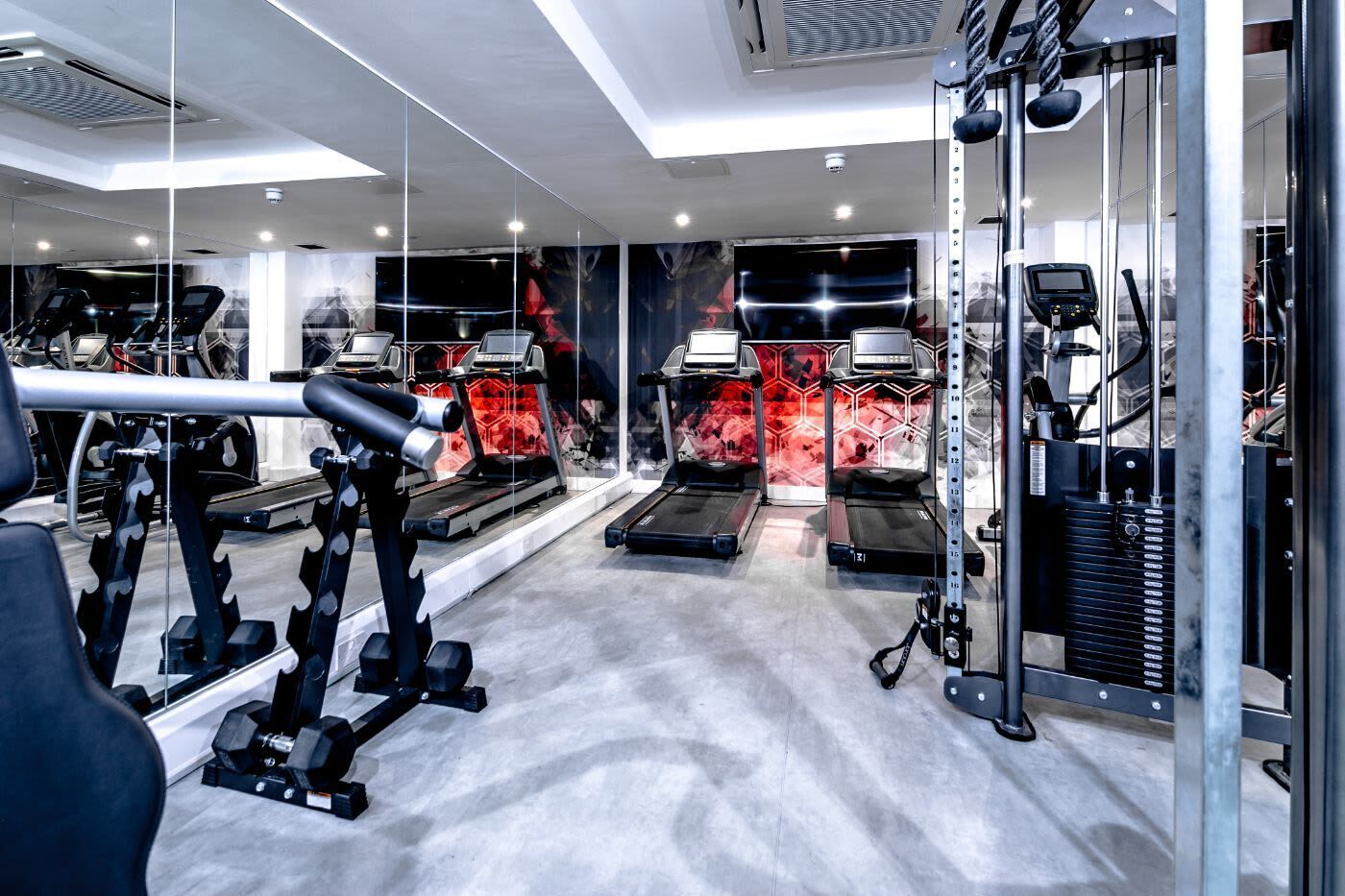 A modern gym with treadmills, weight machines, and a mirrored wall.