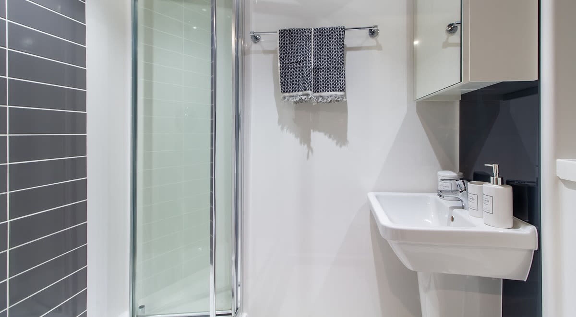 A modern bathroom with a glass shower enclosure, a white sink, and a towel rack with a patterned towel.