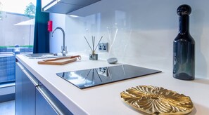 A modern kitchen with a white countertop, a black tablet, a gold decorative plate, a black bottle, and a red fire extinguisher.