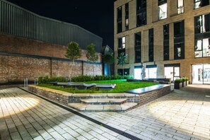 An outdoor area with a paved walkway, a grassy garden, and a building with multiple windows.