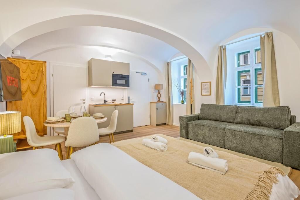 A hotel room with a bed, a sofa, a dining table, and a kitchenette.