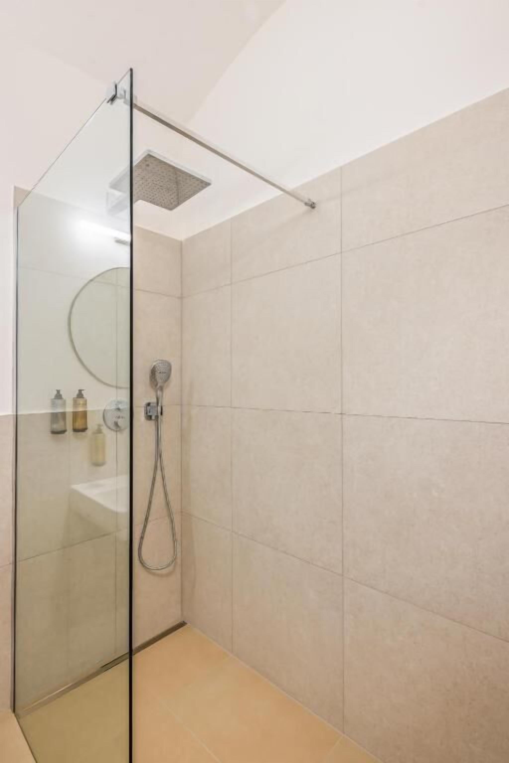 Ducha con mampara de vidrio, cabezal de ducha de mano y panel de control en la pared.