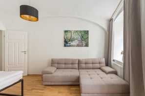 A room with a sectional sofa, a painting of a forest path, a white door, and a window with curtains. - cityswap- Wien Naschmarkt 2 (Wien)