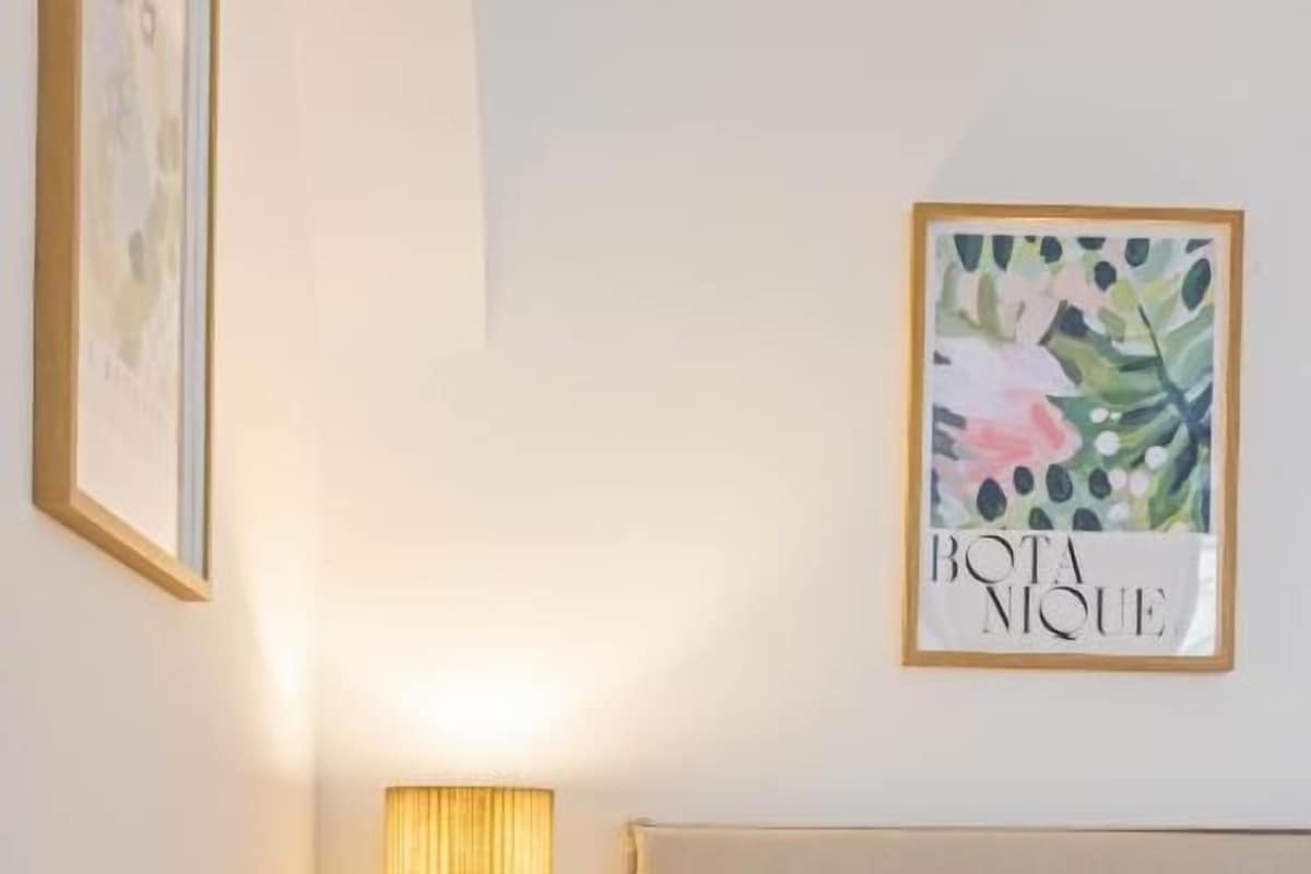 A neatly made bed with a white comforter and a rolled white towel, a bedside lamp on a wooden nightstand, and a framed artwork on the wall.