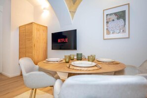 Espaço de refeições com mesa redonda, cadeiras e uma televisão exibindo 'NETFLIX'.