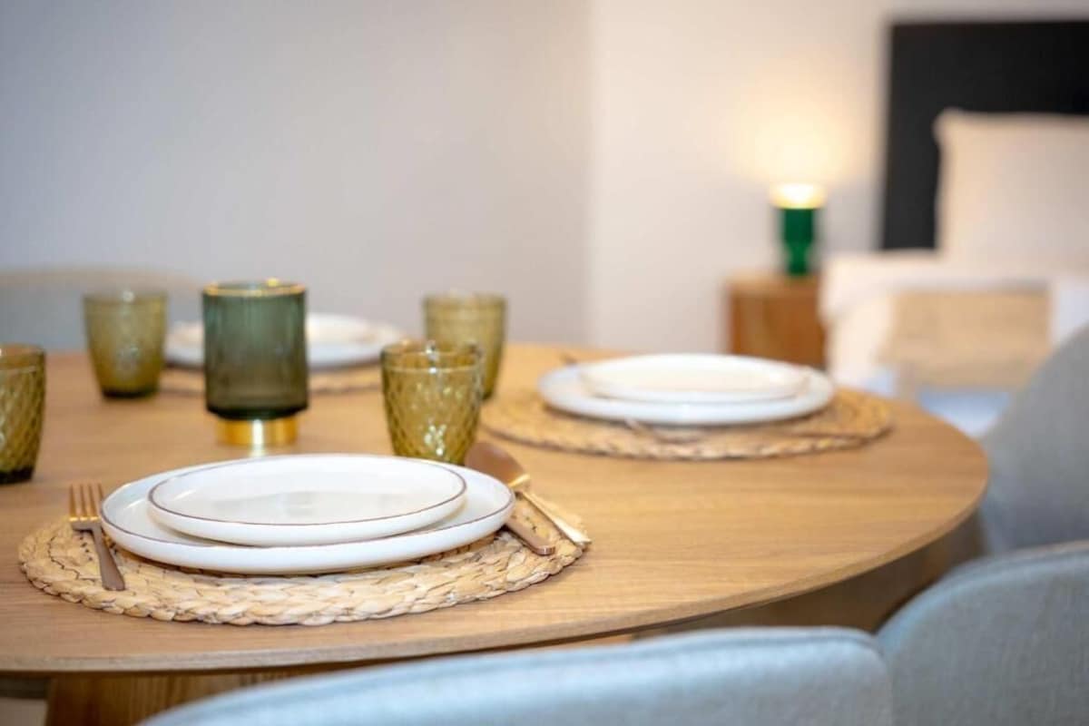 A dining table set with plates, cutlery, and glassware, with a lamp in the background.
