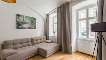 Una sala de estar moderna con un sofá modular, un cuadro de un arroyo en un bosque, un ventanal con cortinas y una lámpara de pie.