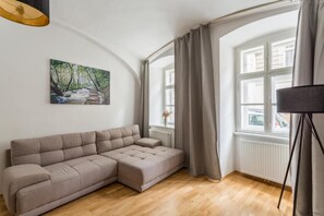 Un saló modern amb un sofà modular, un quadre d'un rierol boscós, una finestra gran amb cortines i una làmpada de peu.
