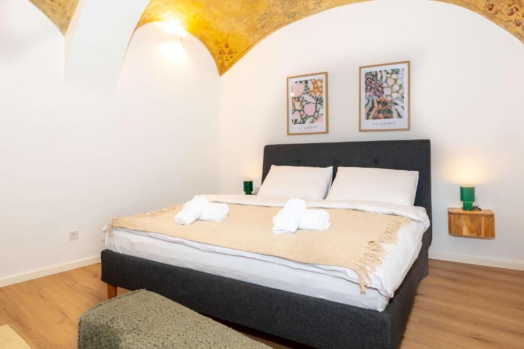 A bedroom with a bed, two wall-mounted lamps, and two framed pictures on the wall.