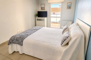 Ein Schlafzimmer mit einem Bett, einem Fernseher auf einer Kommode und einem Fenster mit Blick auf Gebäude.