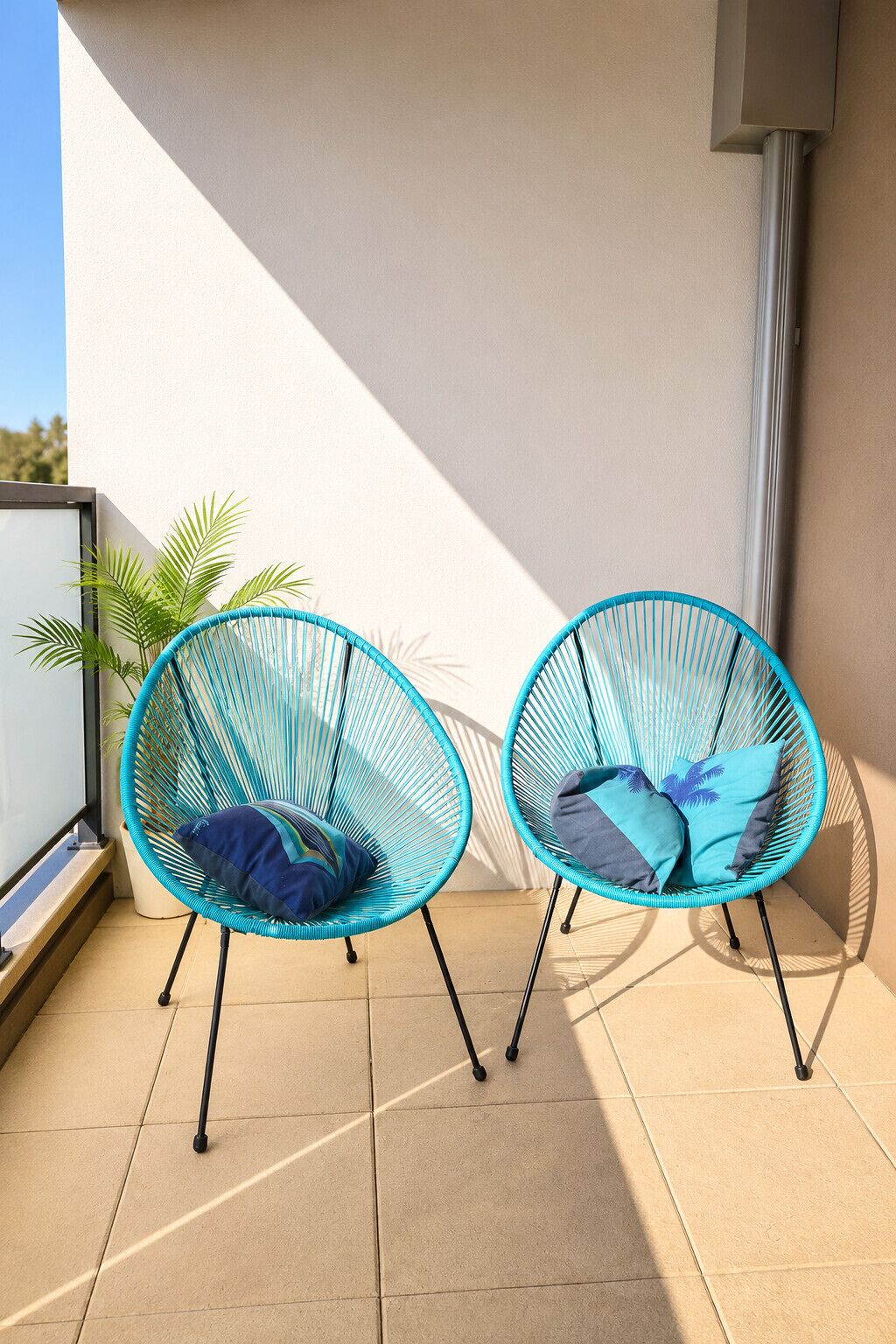 Two blue wire-framed chairs with cushions on a balcony with a tiled floor.