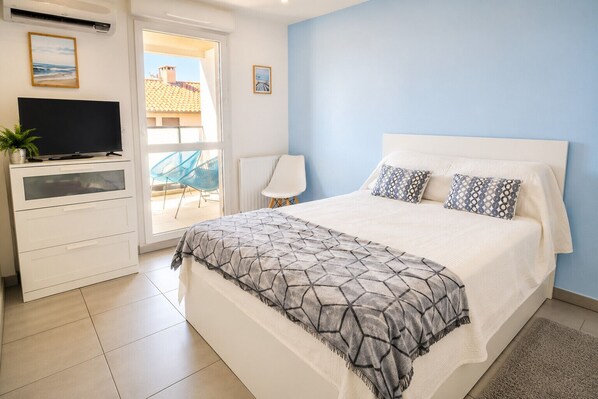 Ein Schlafzimmer mit Bett, Fernseher auf einer Kommode, einem Sessel und Blick ins Freie.