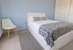 A bedroom with a bed, a chair, and a radiator. - Résidence Cœur Marin : T2 climatisé avec terrasse et parking proche plage (Le Grau-du-Roi)