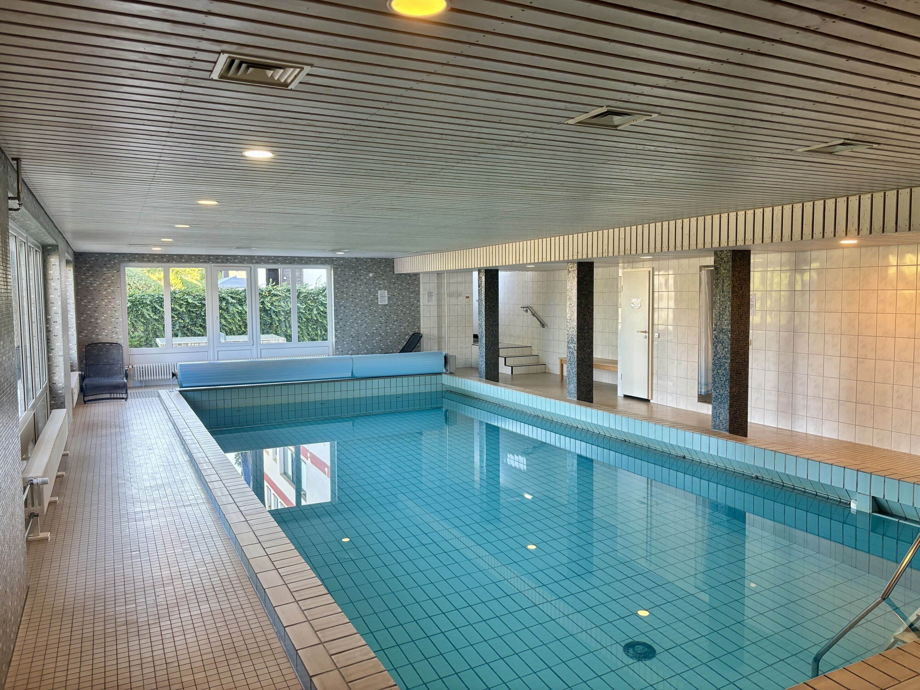 An indoor swimming pool with tiled walls and a bench along the side.