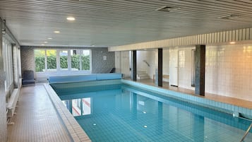 An indoor swimming pool with tiled walls and a bench along the side.