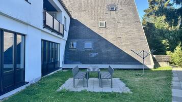 A modern building with a sloped roof, a balcony, and a grassy area with two benches.