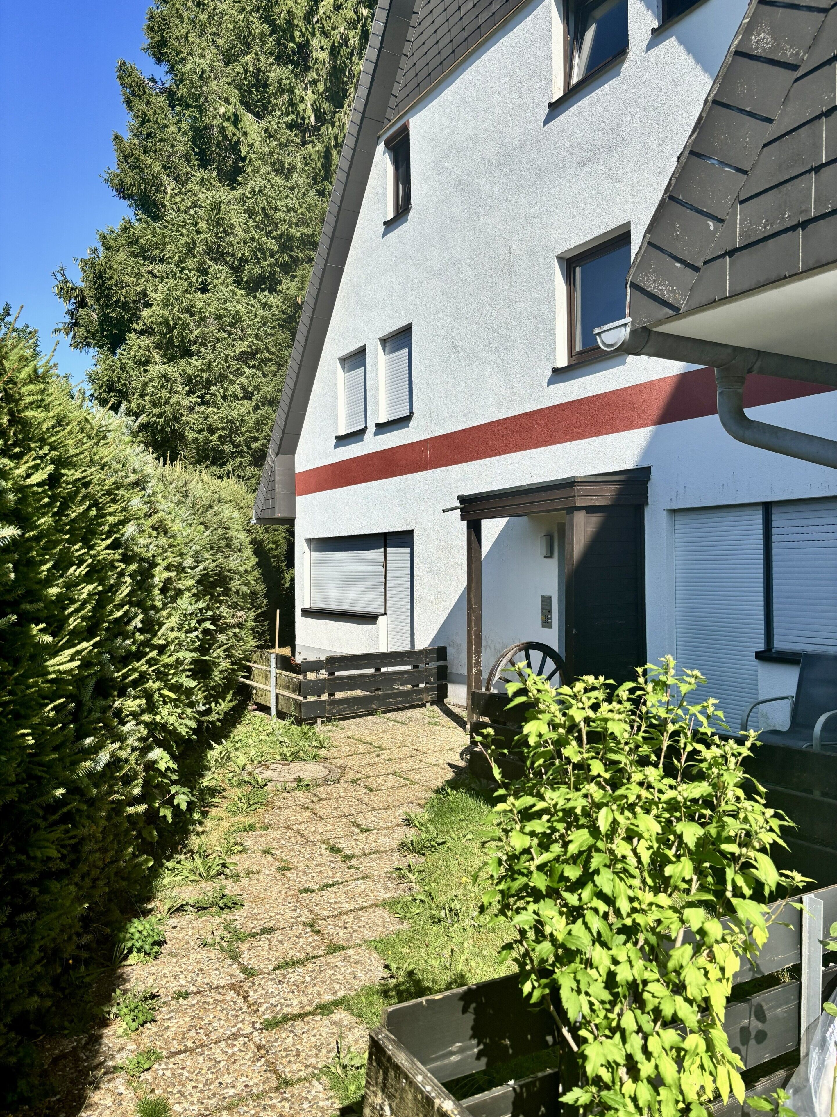 A two-story building with a sloped roof, a garage, and a small garden area with a wooden bench and a wheelbarrow.