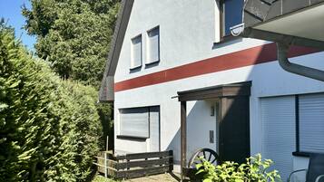 A two-story building with a sloped roof, a garage, and a small garden area with a wooden bench and a wheelbarrow.