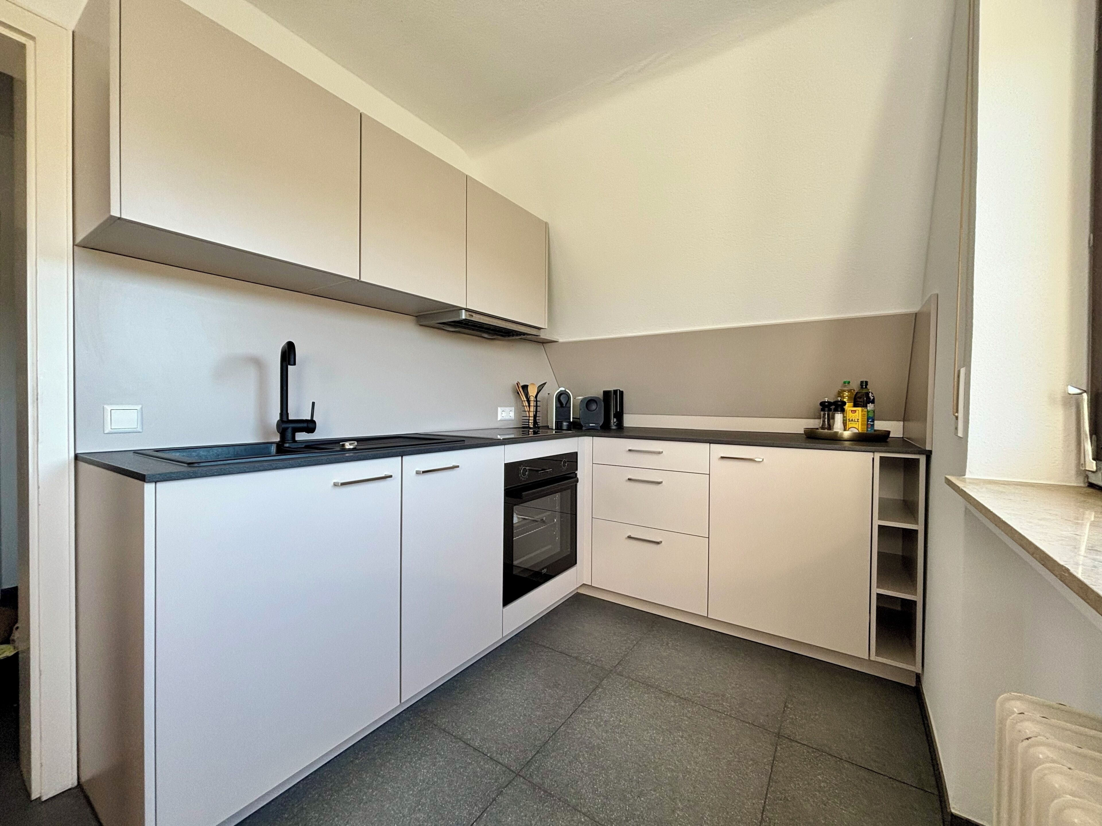 A modern kitchen with white cabinets, a black countertop, a built-in oven, and a stainless steel range hood.