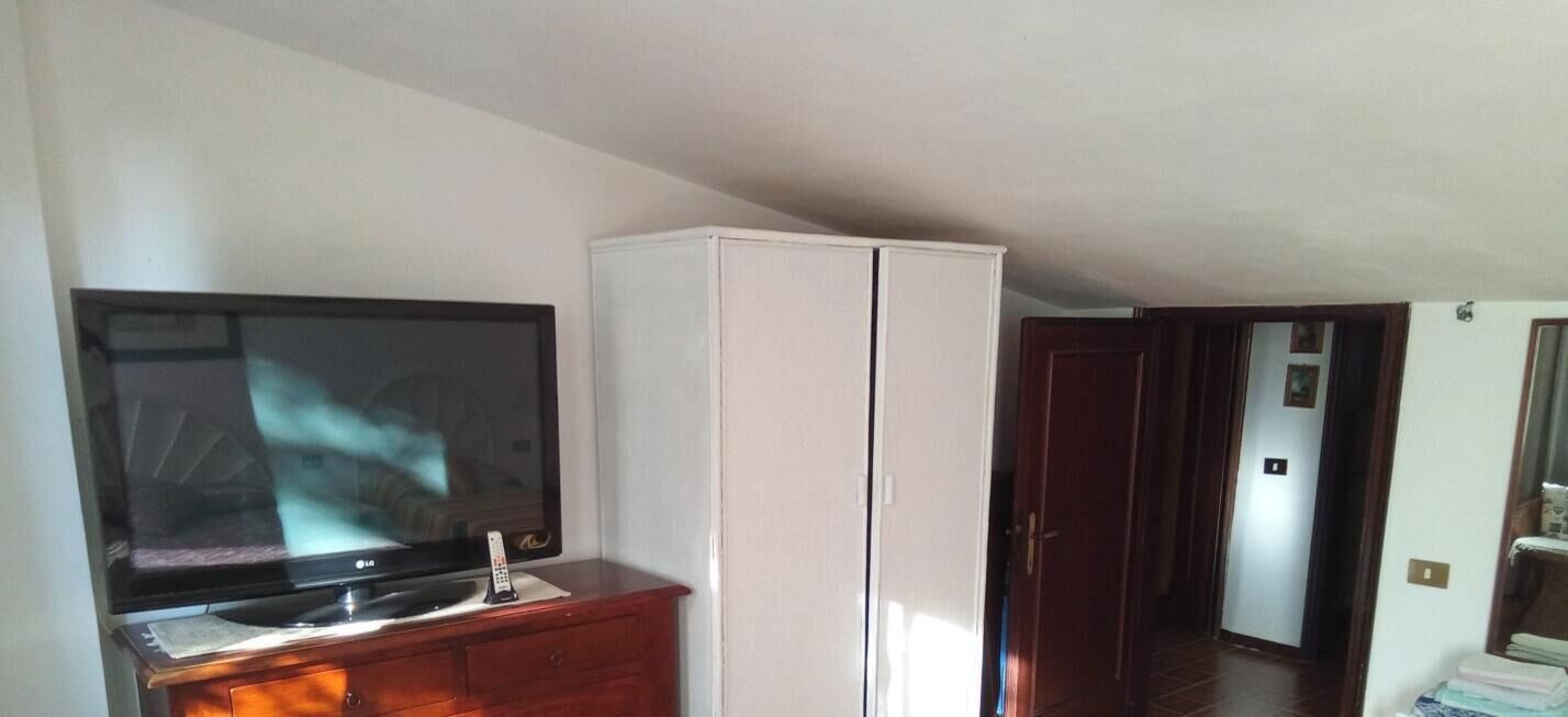 Une pièce avec un téléviseur posé sur un meuble en bois, une armoire blanche et une porte donnant sur une autre pièce.