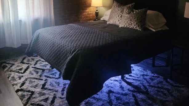 A bedroom with a bed, a ceiling fan, a lamp, and a brick wall.