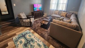 A living room with a sofa, armchair, coffee table, and a TV on a stand.