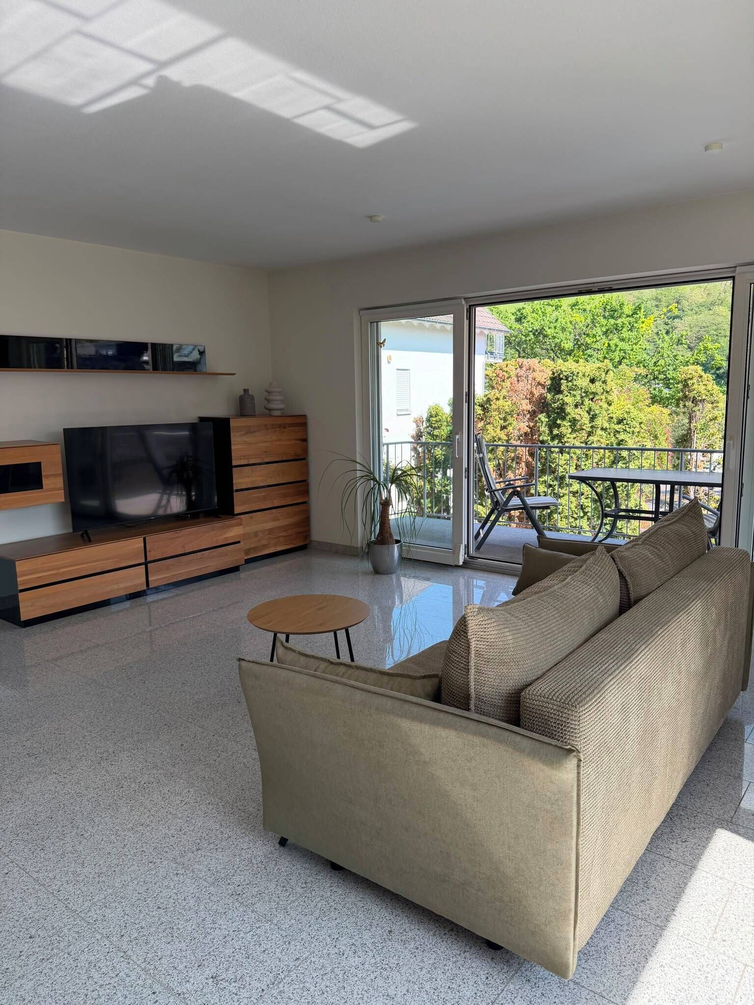 Een moderne woonkamer met een bank, televisie en een balkon met tuinmeubilair.