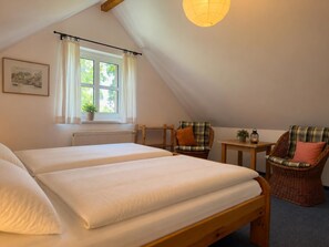 Een slaapkamer met twee bedden, een raam met gordijnen, een stoel, een klein tafeltje en een hanglamp.