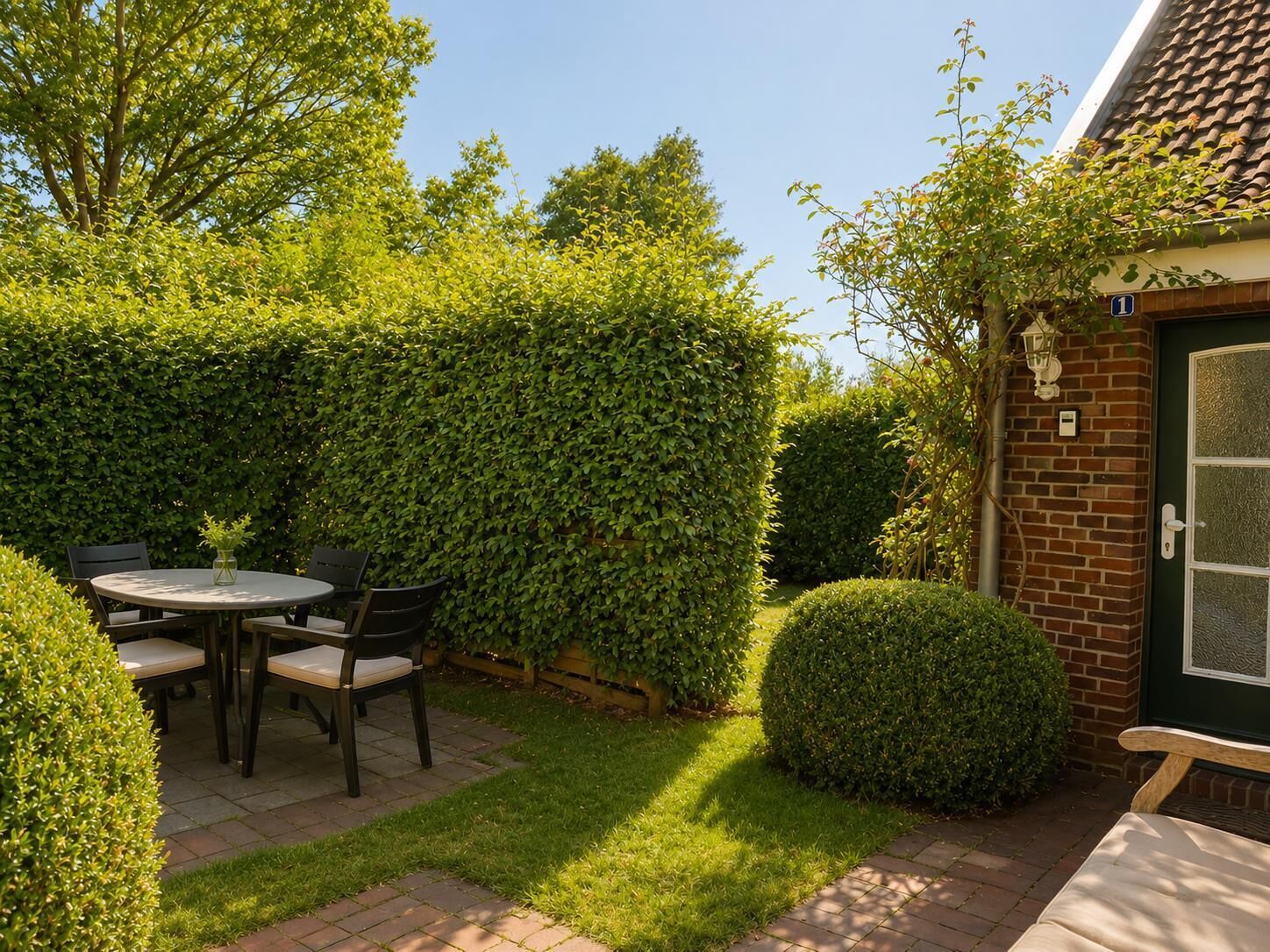 A patio with a round table and chairs, surrounded by well-maintained hedges and a brick wall.