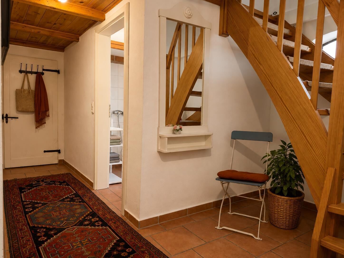 Un escalier avec des rampes en bois menant à l’étage supérieur, un petit banc avec un coussin, une plante en pot et un tapis à motifs sur le sol.
