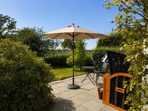 An outdoor patio with a table and chairs, a large umbrella, and a garden view. - A cozy vacation home right on Lake Wangermeer, sleeping up to 4 people, with two bedrooms, two bathrooms, and plenty of space to relax in the idyllic town of Gottels near Hohenkirchen. (Wangerland)