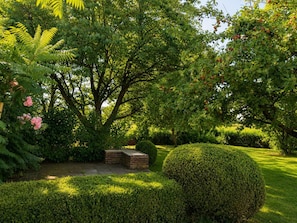 Ein gepflegter Garten mit verschiedenen Bäumen, einer ordentlich geschnittenen Hecke und einem Kiesweg.