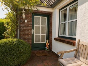 Een bakstenen huis met een groene deur, een raam met een witte omlijsting, een houten bankje en een klein decoratief beeldje.