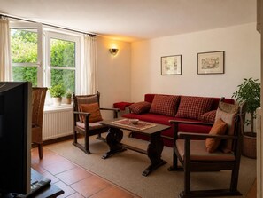 Een woonkamer met een rode bank, twee fauteuils, een salontafel en een televisie.