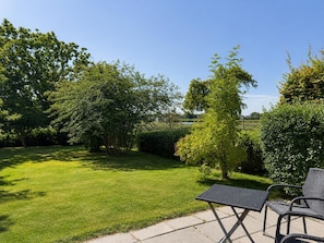 Ein Terrassenbereich mit Tisch und Stühlen, umgeben von einem gepflegten Rasen und verschiedenen Bäumen.