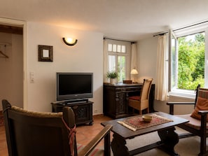 Ein Wohnzimmer mit Fernseher, einem Esstisch und einem fenster mit Vorhängen.