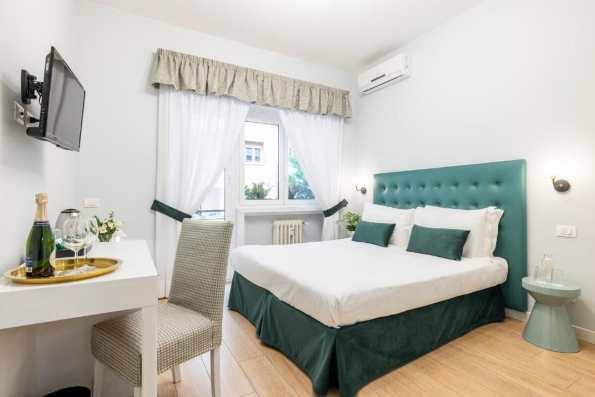 Una habitación de hotel con una cama, un escritorio con silla, un televisor y una ventana con cortinas.