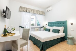 Una habitación de hotel con una cama, un escritorio con silla, un televisor y una ventana con cortinas.