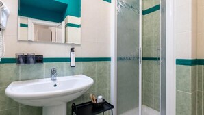 A bathroom with a sink, a mirror, a shower enclosure, and a hairdryer.