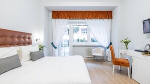 A bedroom with a bed, a desk, a chair, and a window with curtains.