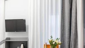 A compact room with a kitchenette, a glass table with a vase and flowers, and a television mounted on the wall.