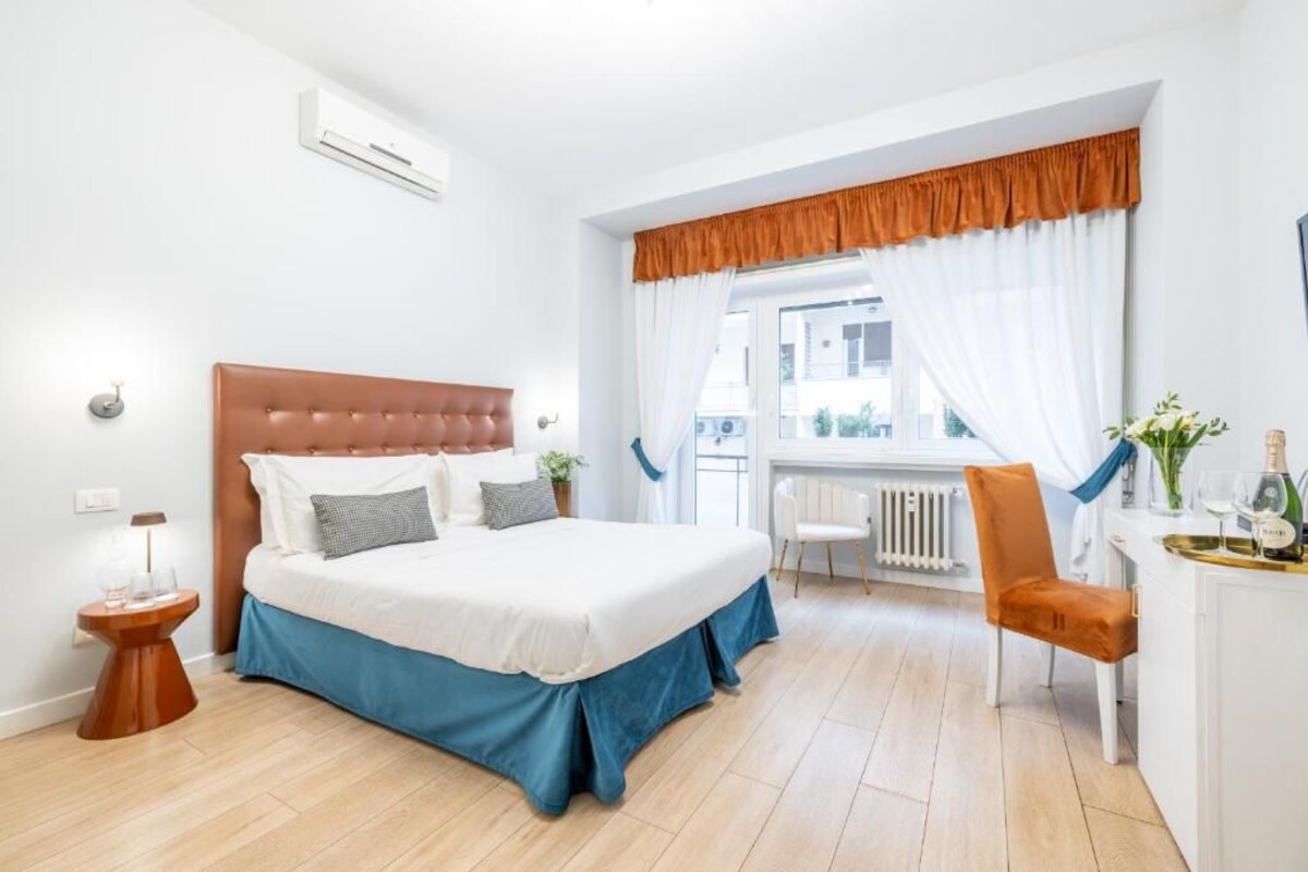 Habitación de hotel con cama, mesita de noche, silla, ventana con cortinas y radiador.