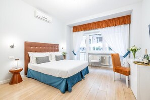 Habitación de hotel con cama, mesita de noche, silla, ventana con cortinas y radiador.