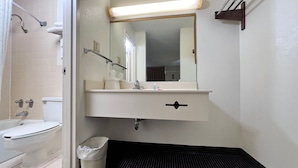 A bathroom with a toilet, sink, mirror, and shower area. - Heritage Inn and Suites (Baton Rouge)