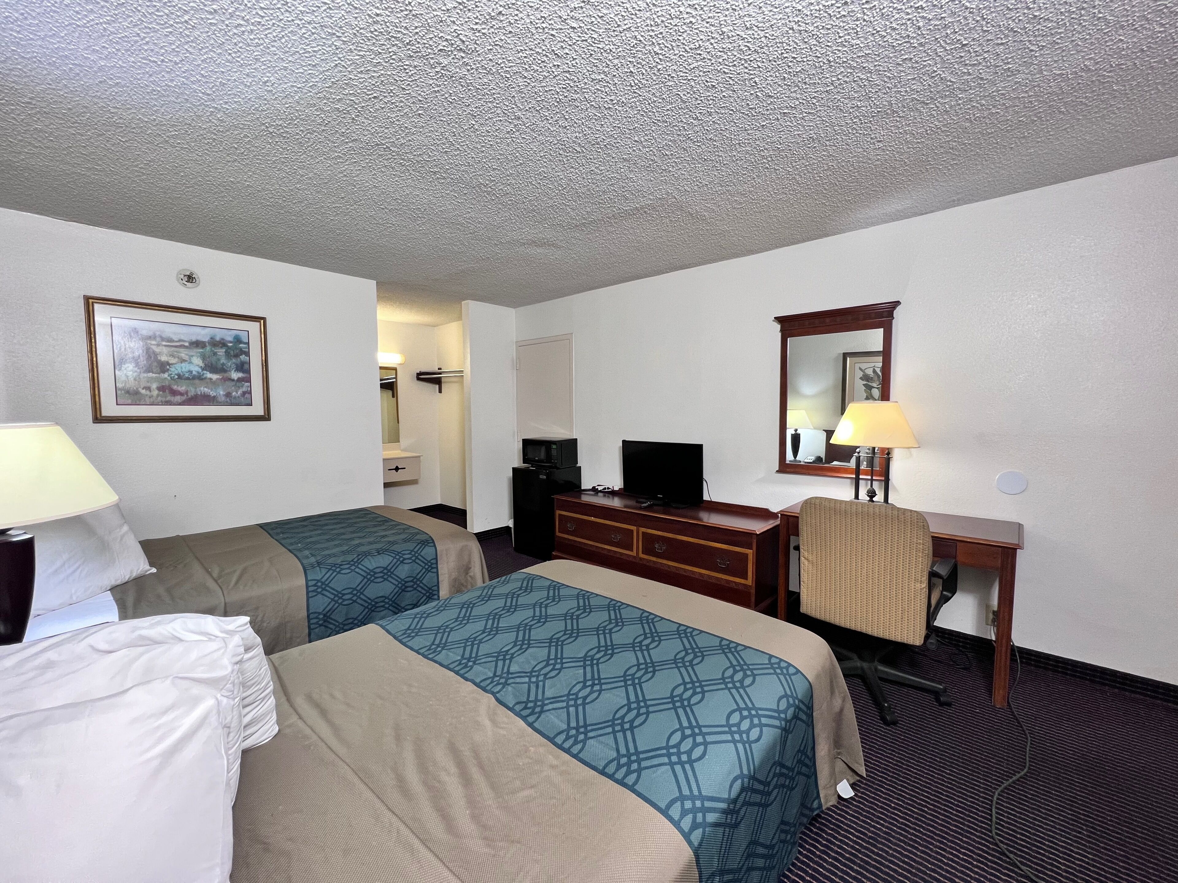 A hotel room with two beds, a desk, a television, and a mirror.