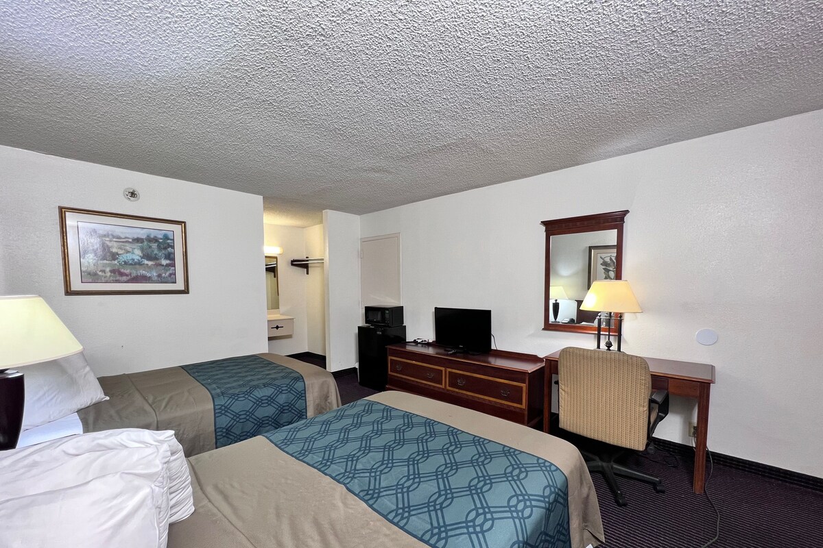 A hotel room with two beds, a desk, a television, and a mirror.