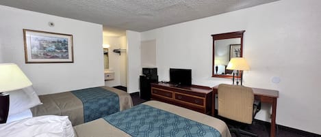 A hotel room with two beds, a desk, a television, and a mirror.