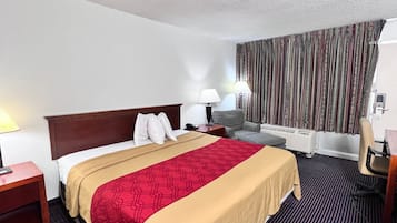 Habitación de hotel con una cama grande, un escritorio, una silla, una lámpara y una ventana con cortinas.
