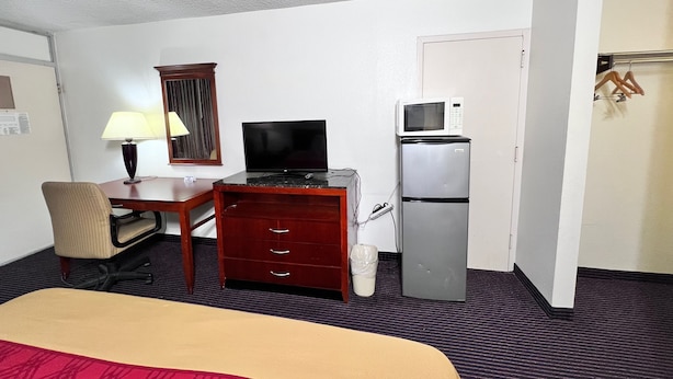 Una habitación de hotel con cama, escritorio, computadora, televisor, microondas y refrigerador.